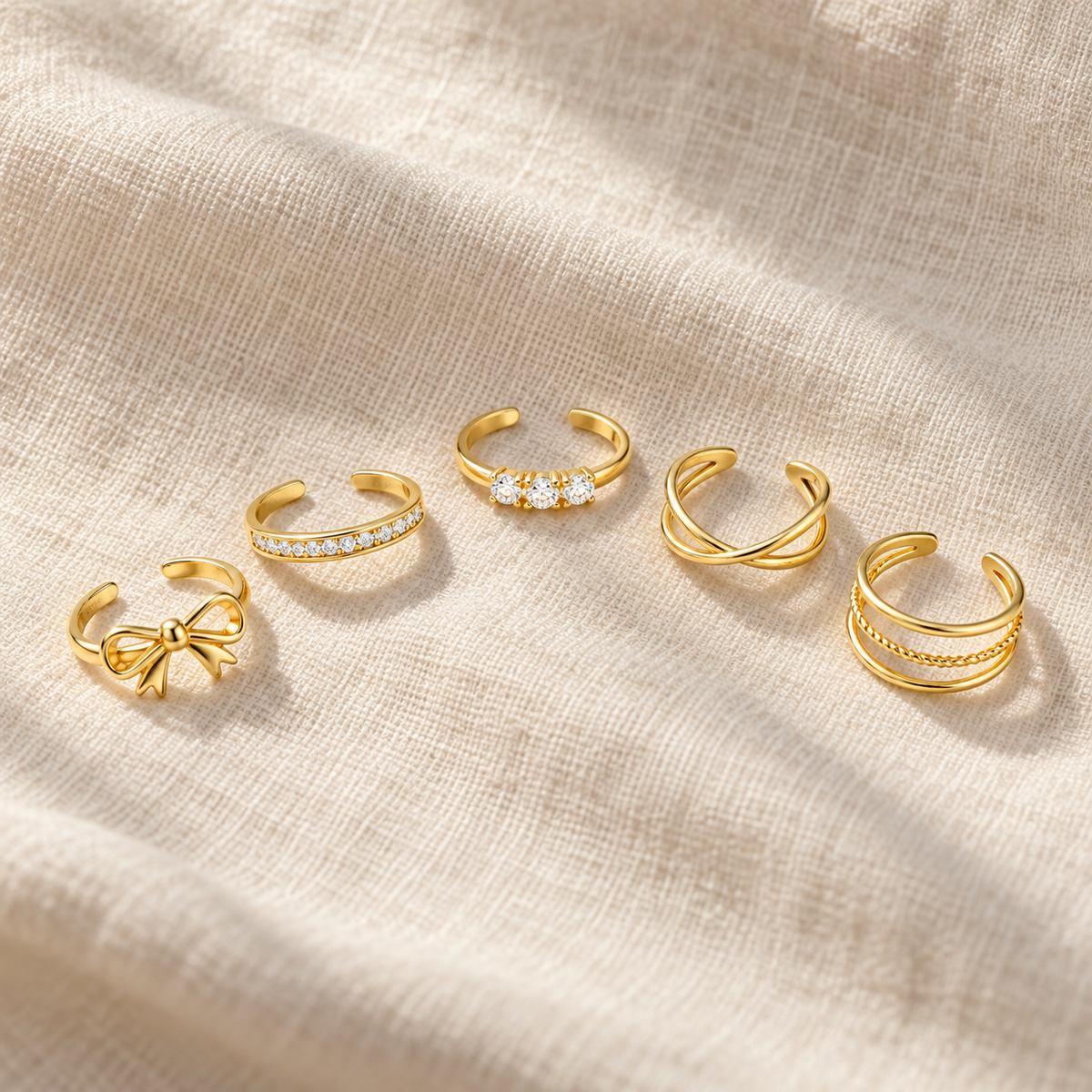 Bow toe ring beside four other gold-tone styles on linen