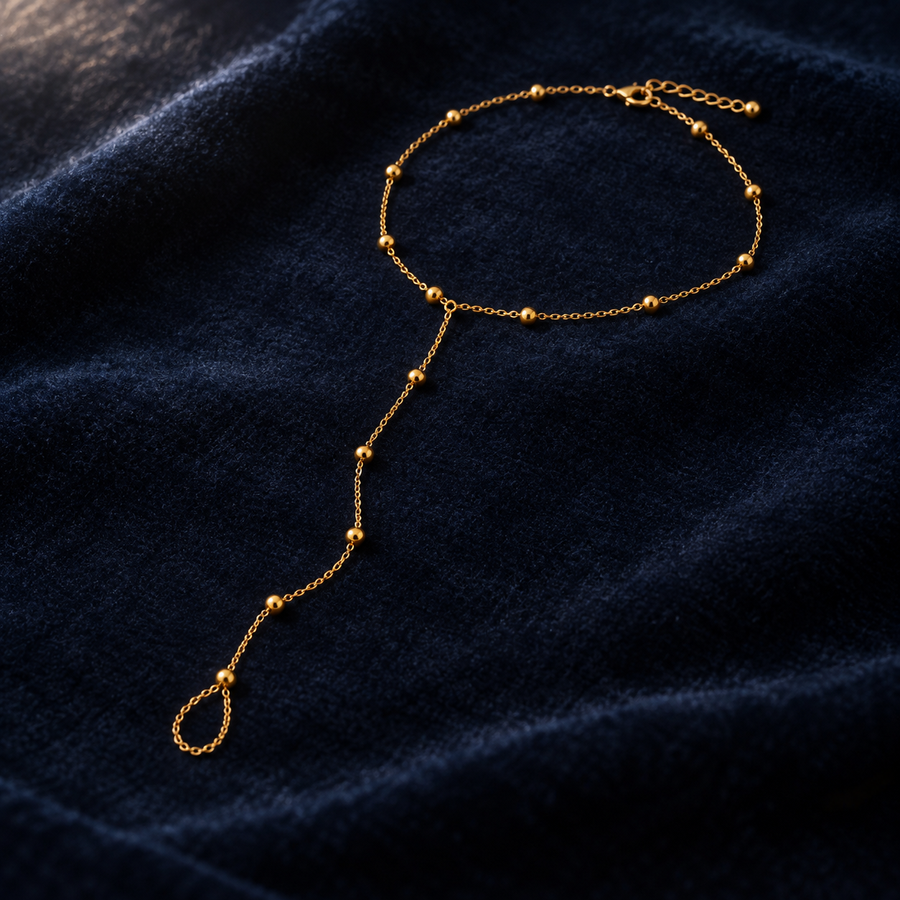 Gold bead barefoot sandal laid on deep navy velvet