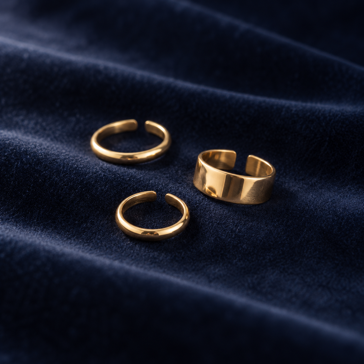 Plain toe ring trio on deep navy velvet: two slim bands and one wide polished band