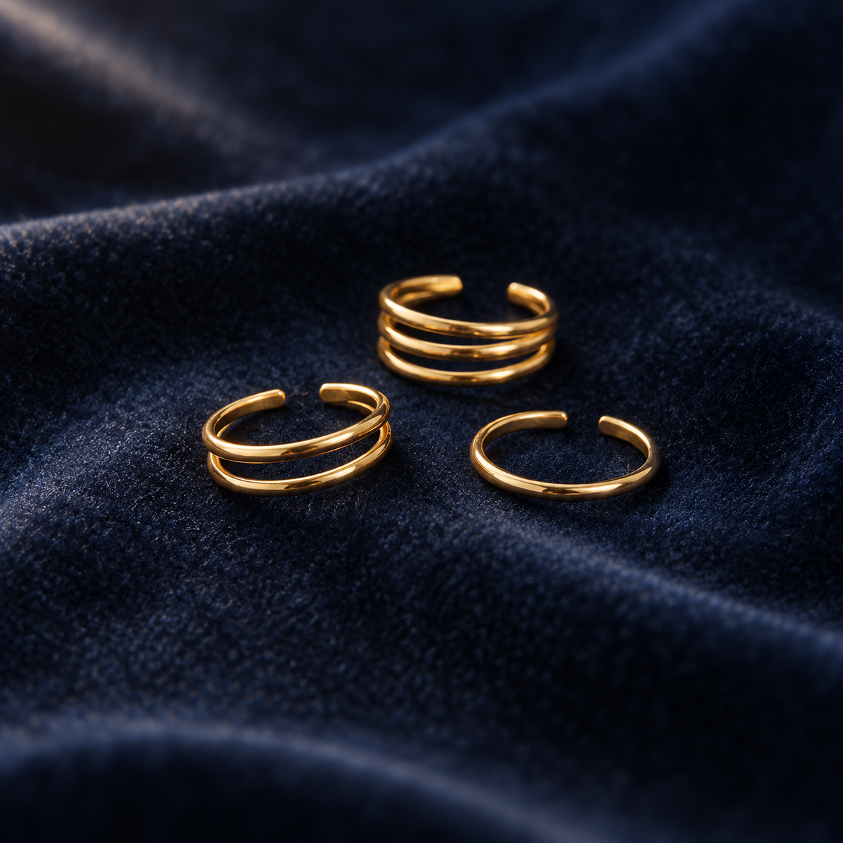 Row toe ring trio on deep navy velvet: a triple-line band, a single band and a double-line band